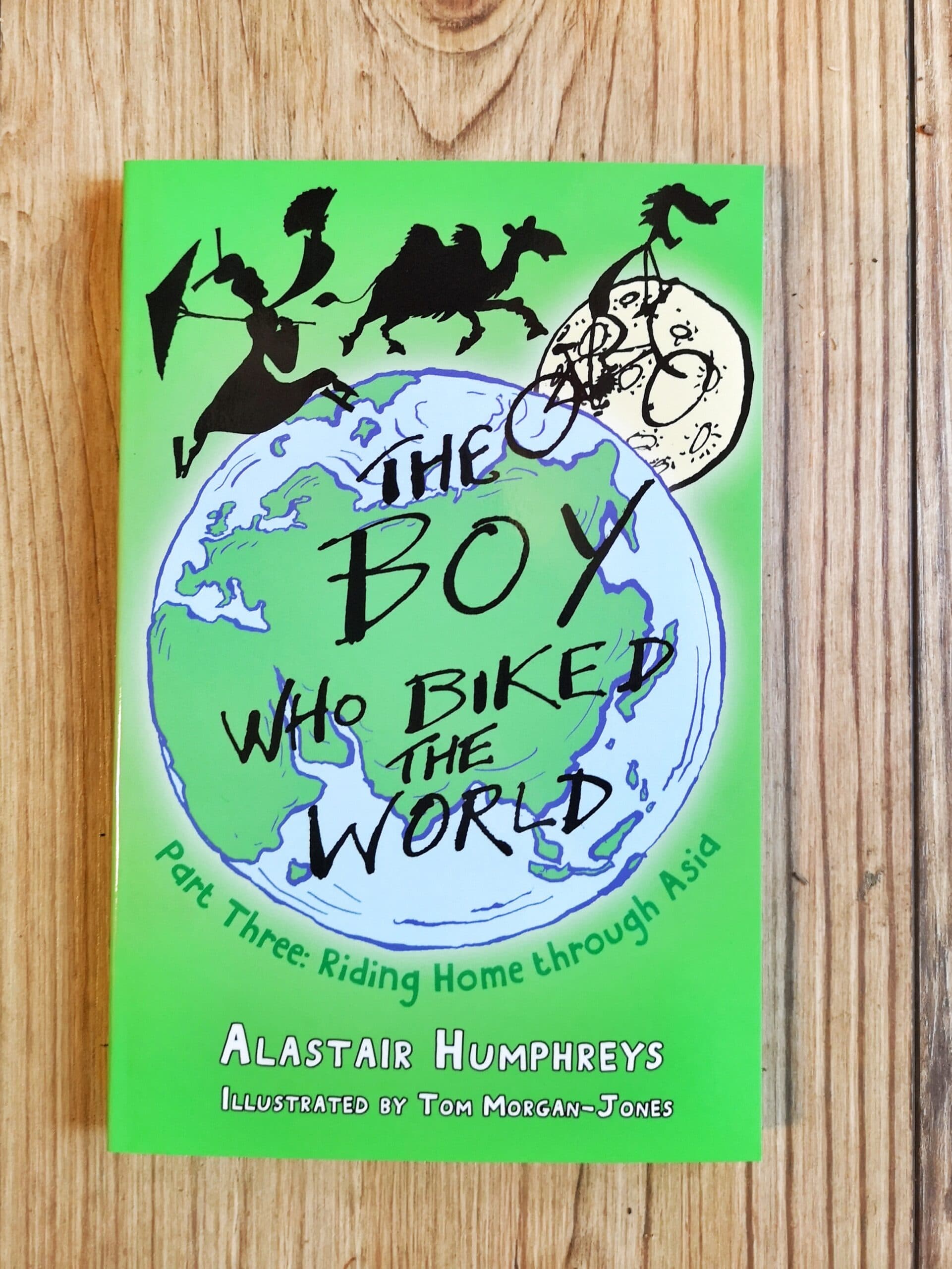 Books by Alastair Humphreys - The Boy Who Biked the World: Part Three: Riding Home Through Asia - Cover on Wooden Floor